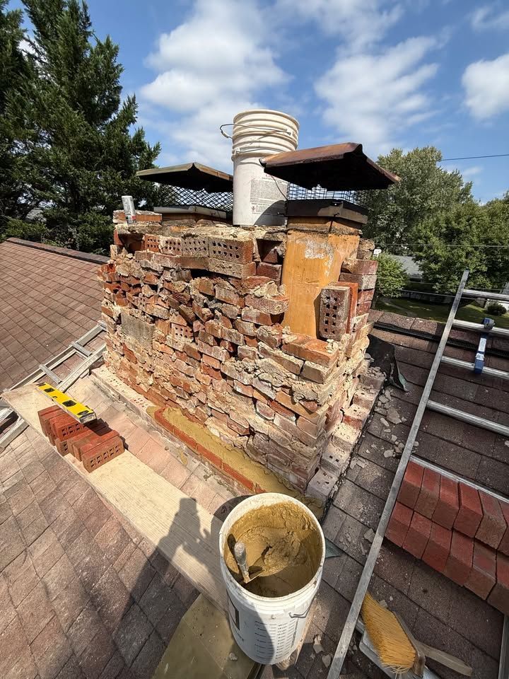 Damaged brick chimney on a rooftop being repaired, with tools and materials nearby.