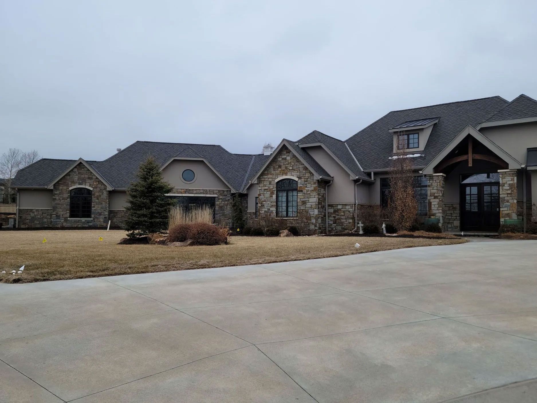 Large house with stone accents, tan walls, and dark roof under a cloudy sky.