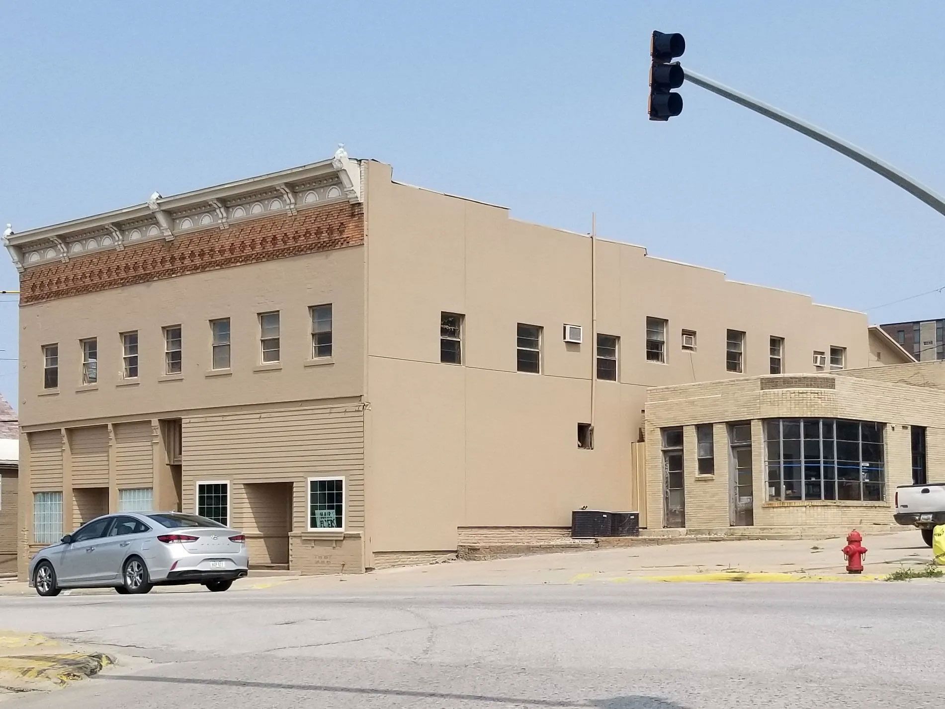 Two-story tan building with a car parked in front, traffic light in the upper right.