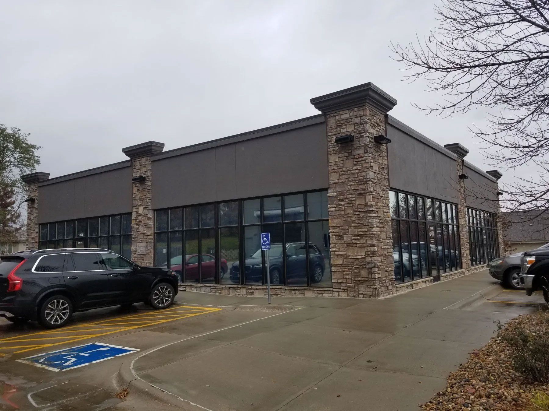 Exterior of a car dealership on an overcast day; dark-colored building with large windows and stone columns.