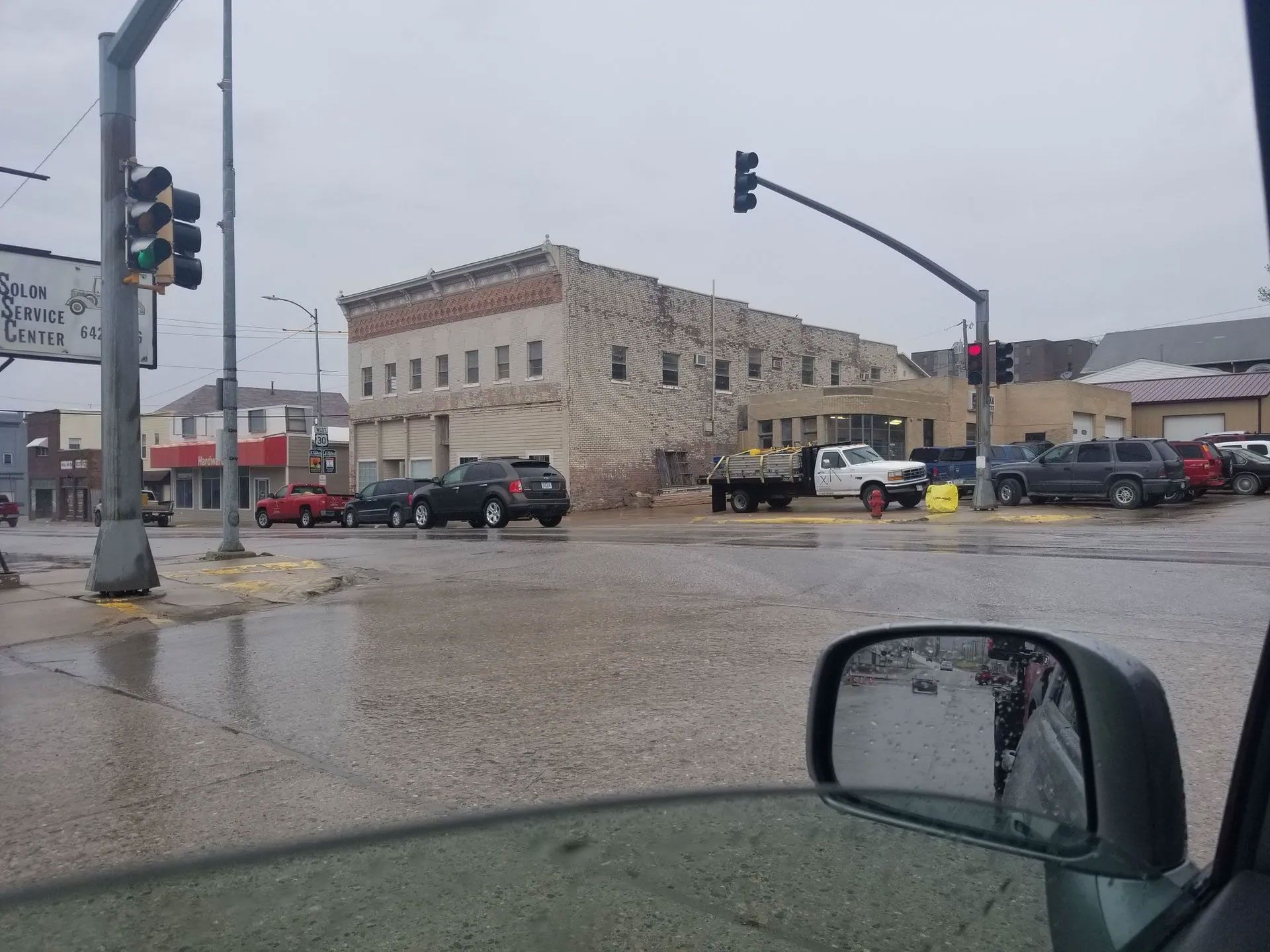 Street scene on a rainy day with a large brick building, cars, and traffic lights.