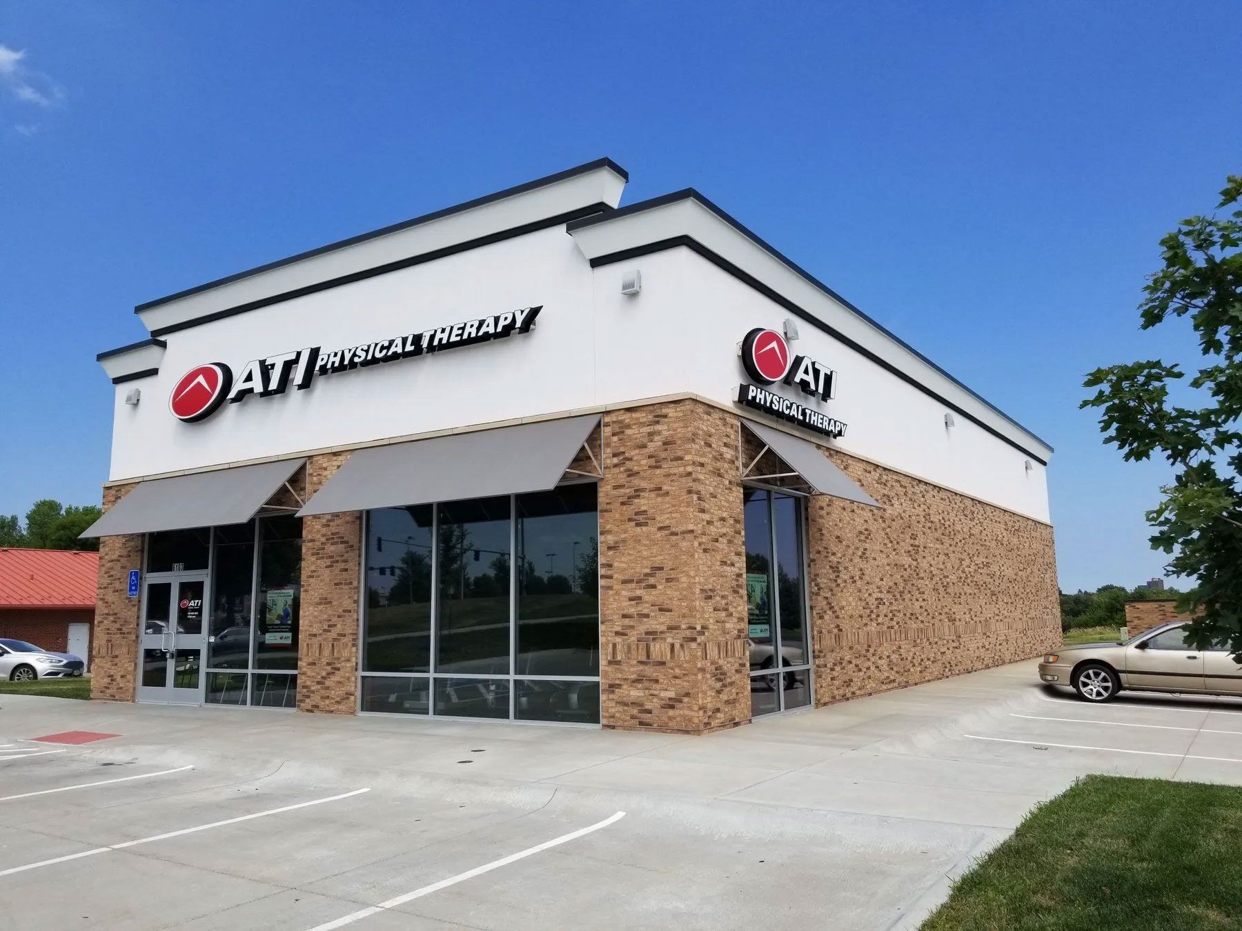 Exterior of an ATI Physical Therapy clinic, white building with tan stone accents, blue sky.