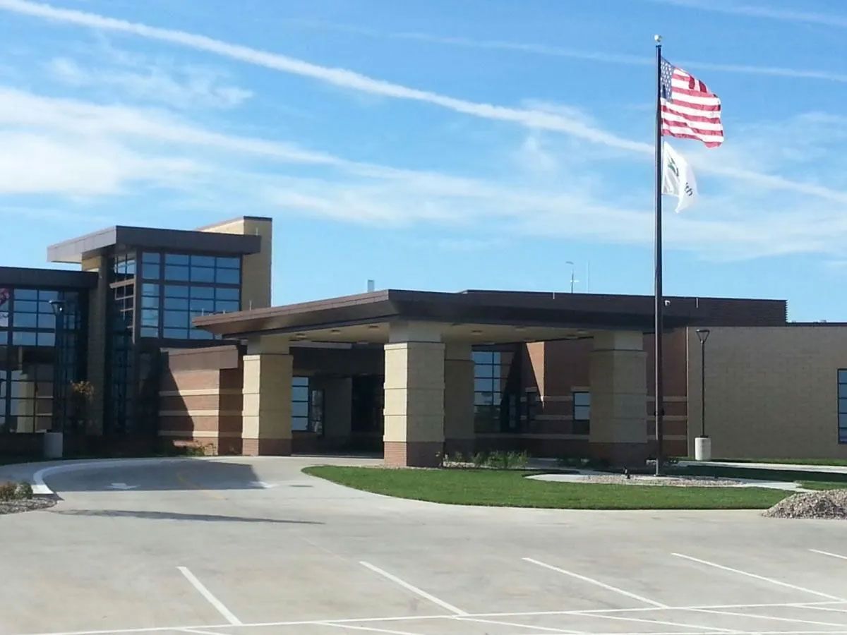 Modern building with glass windows, brown accents, and American flag on a pole under a blue sky.