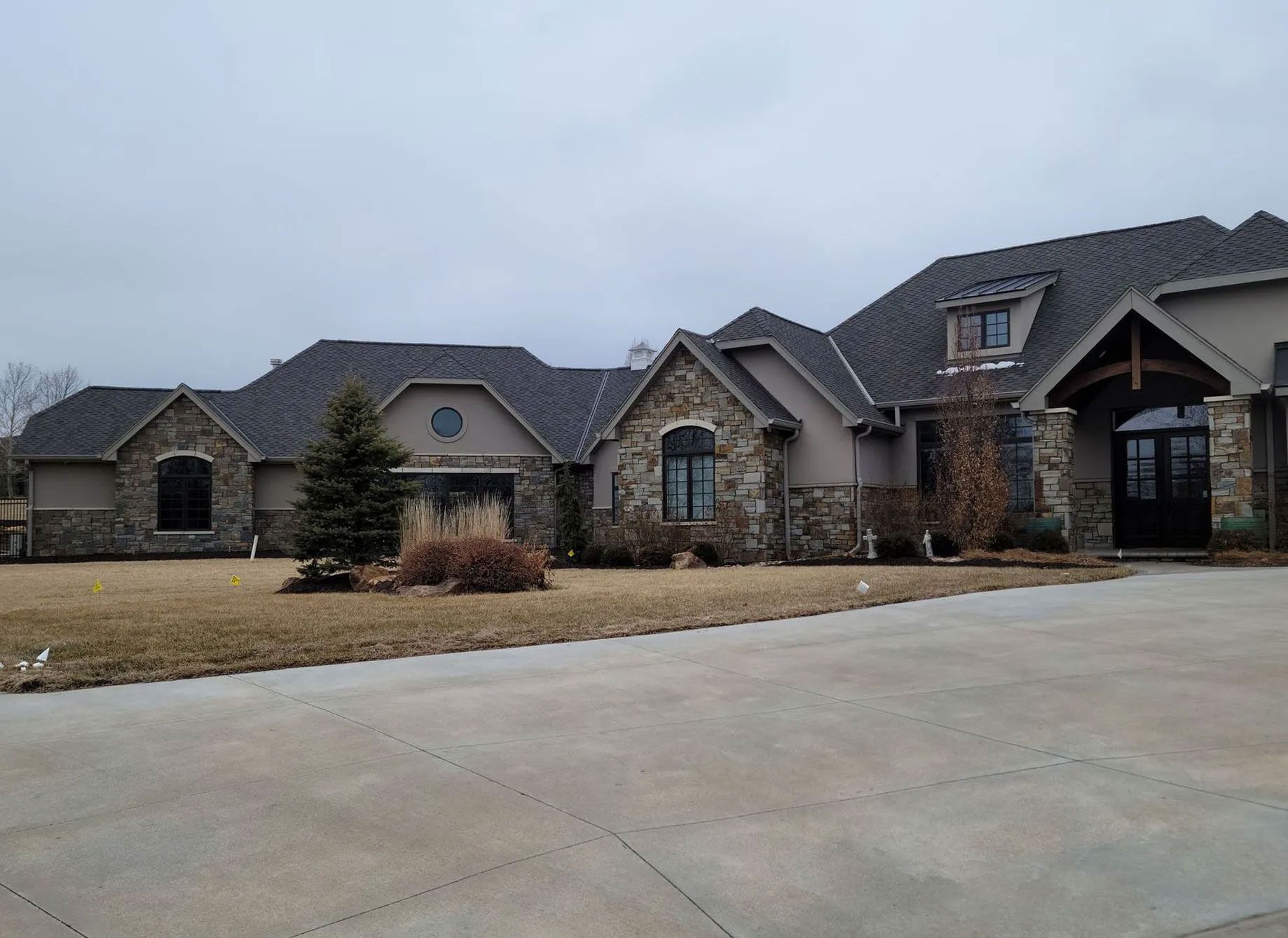 Large stone and stucco house with multiple rooflines, a circular window, and a driveway.