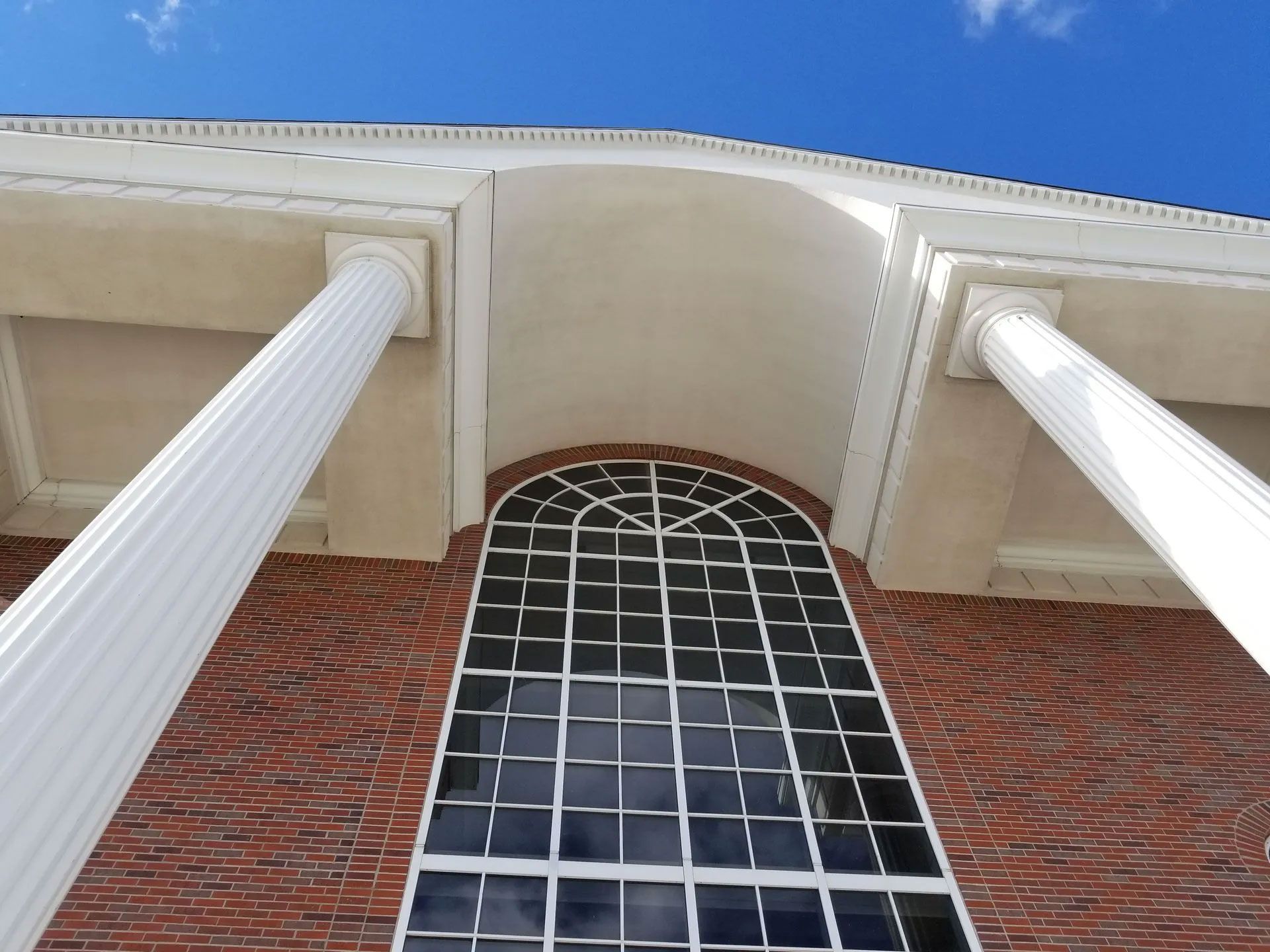 Brick building with large arched window, topped by white columns and a light-colored roof. Blue sky visible.