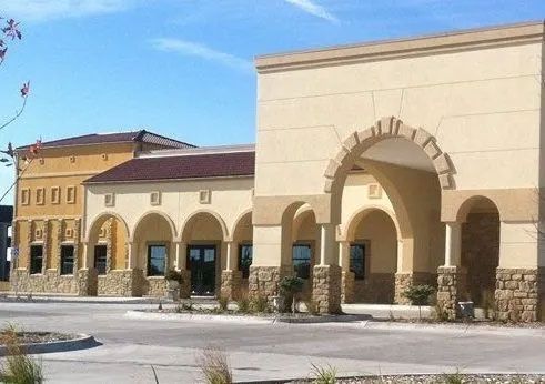 Beige stucco commercial building with arched entrances, tan trim, and stone accents.