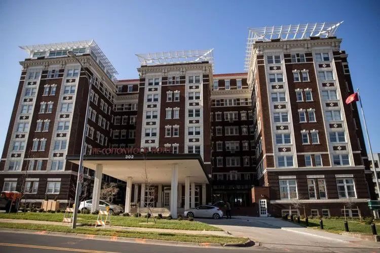 Brown brick apartment building with white accents, entrance awning, and flag.