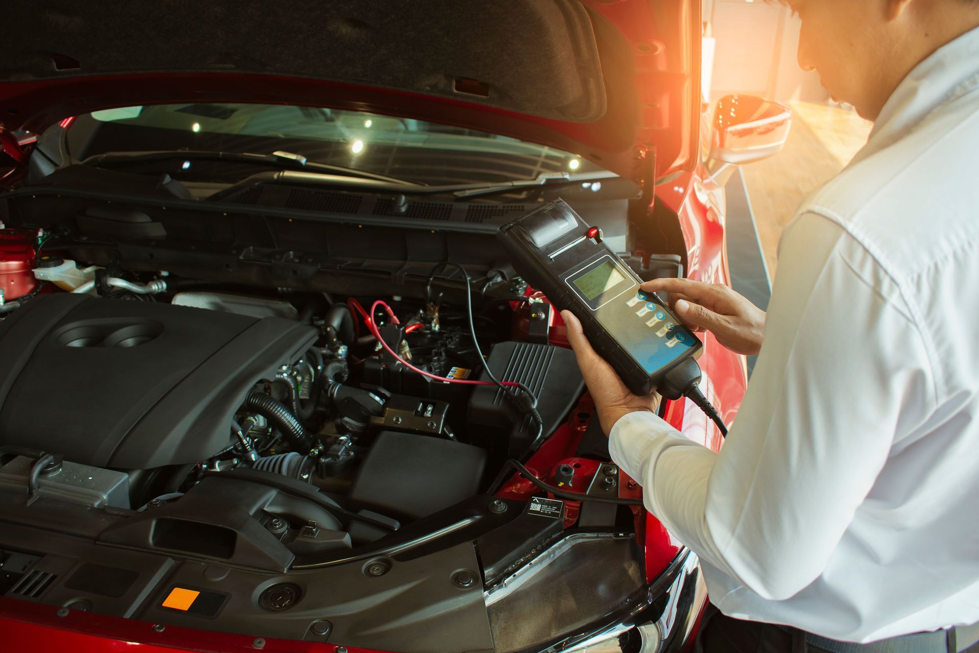 Mechanic uses a diagnostic tool on a red car engine, likely checking the vehicle's systems.
