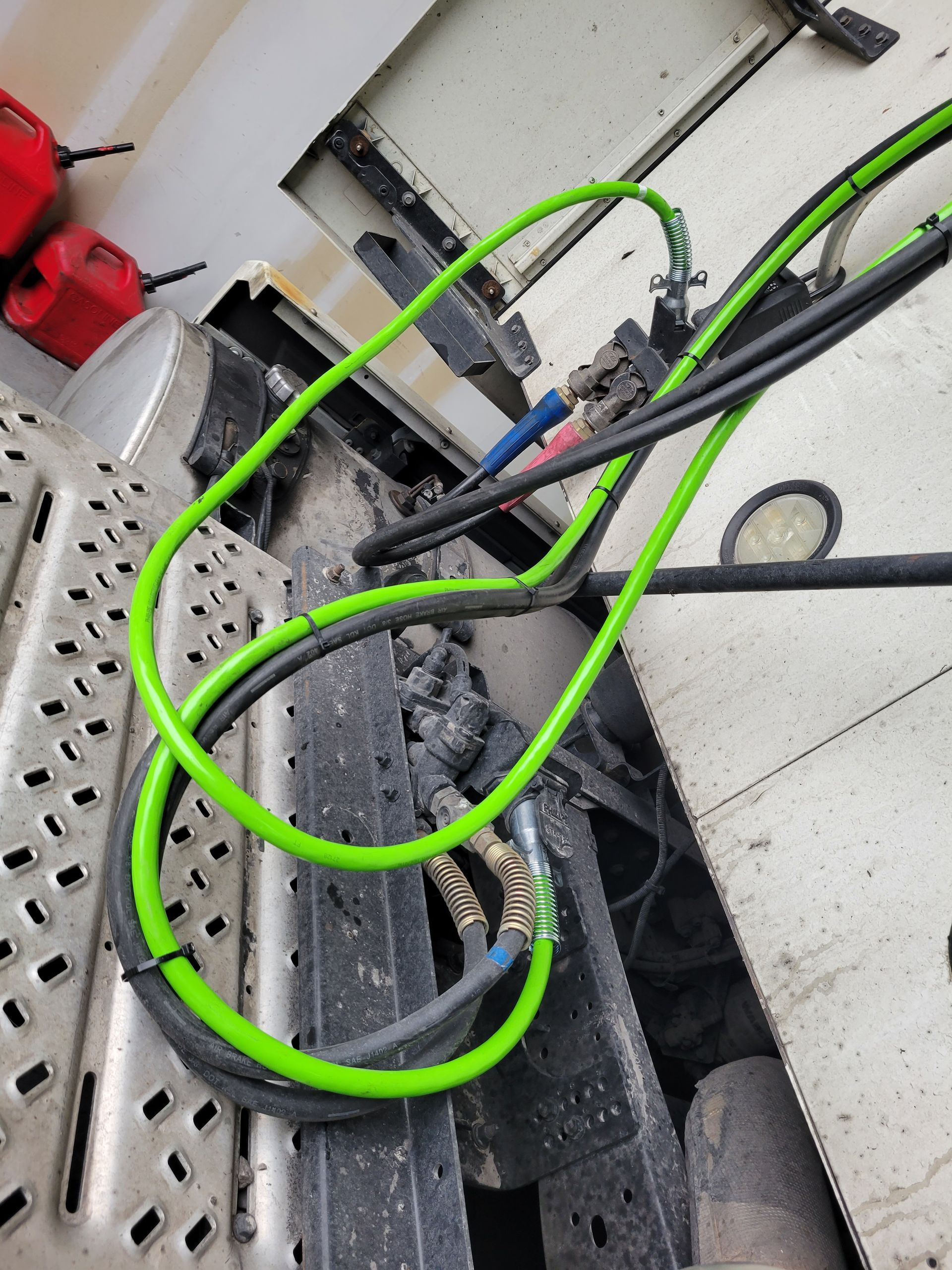 A green hose is hanging from the side of a truck.