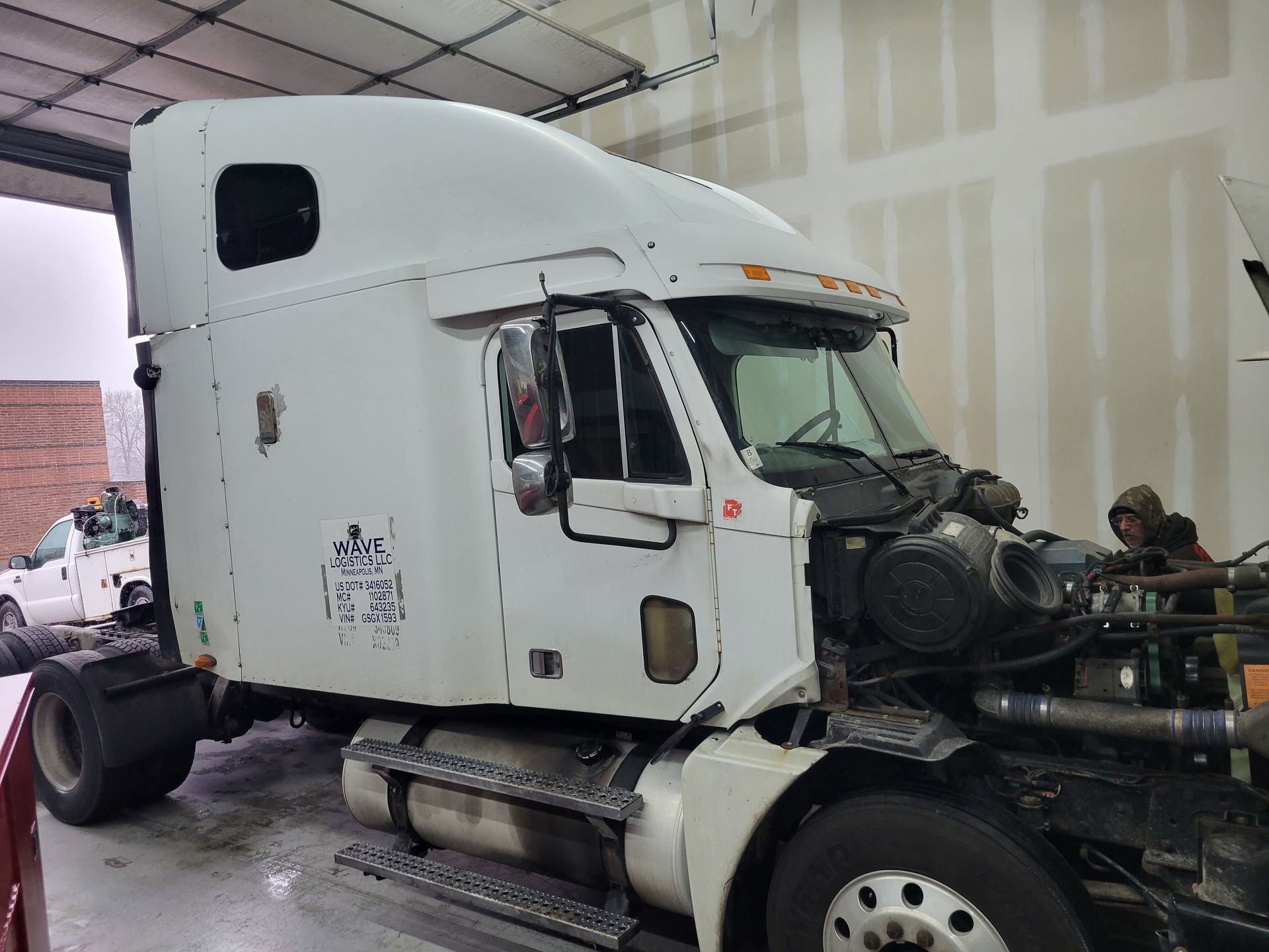 A white semi truck is sitting in a garage with its hood open.