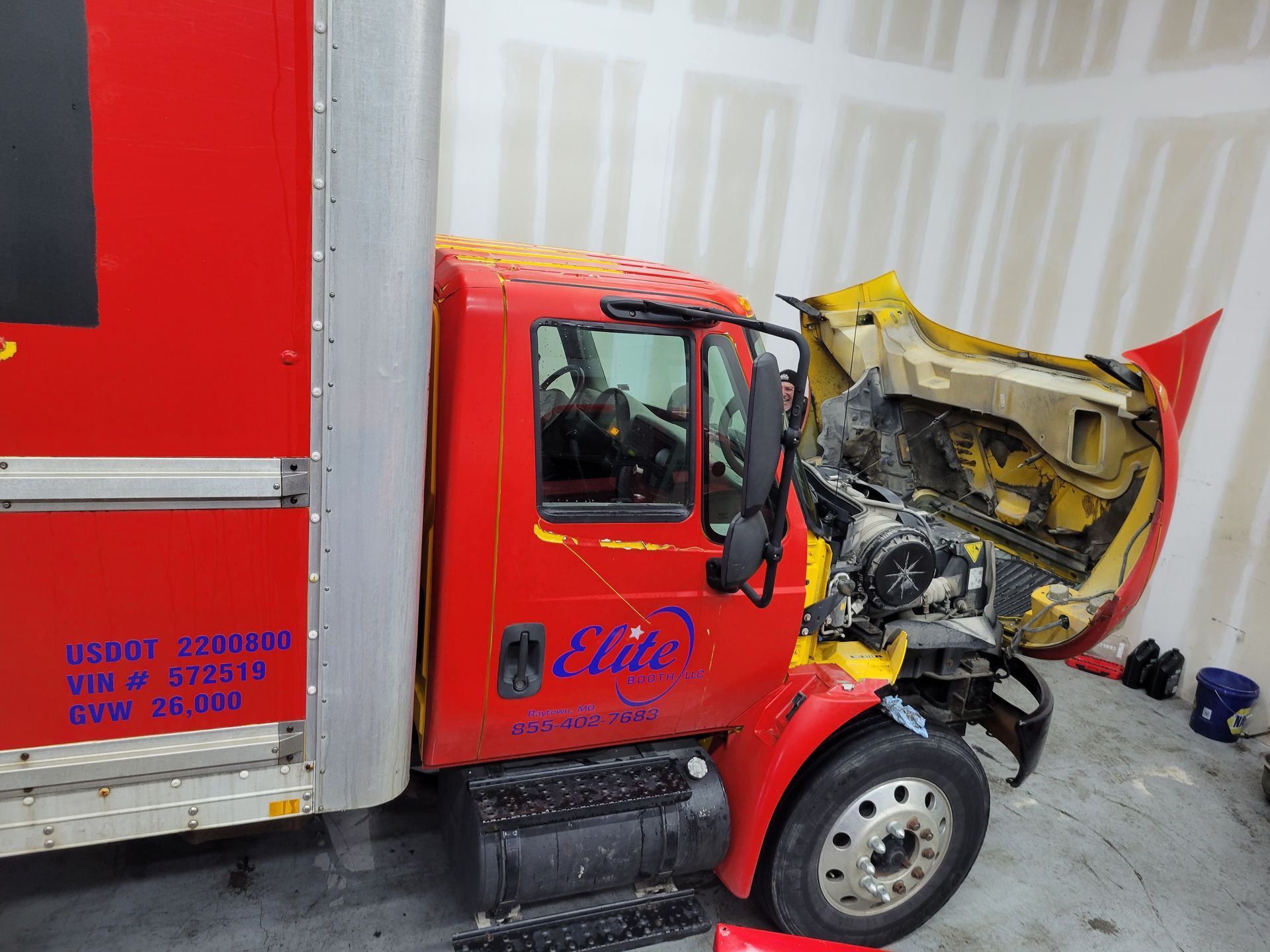 A red truck is sitting in a garage with its hood open.