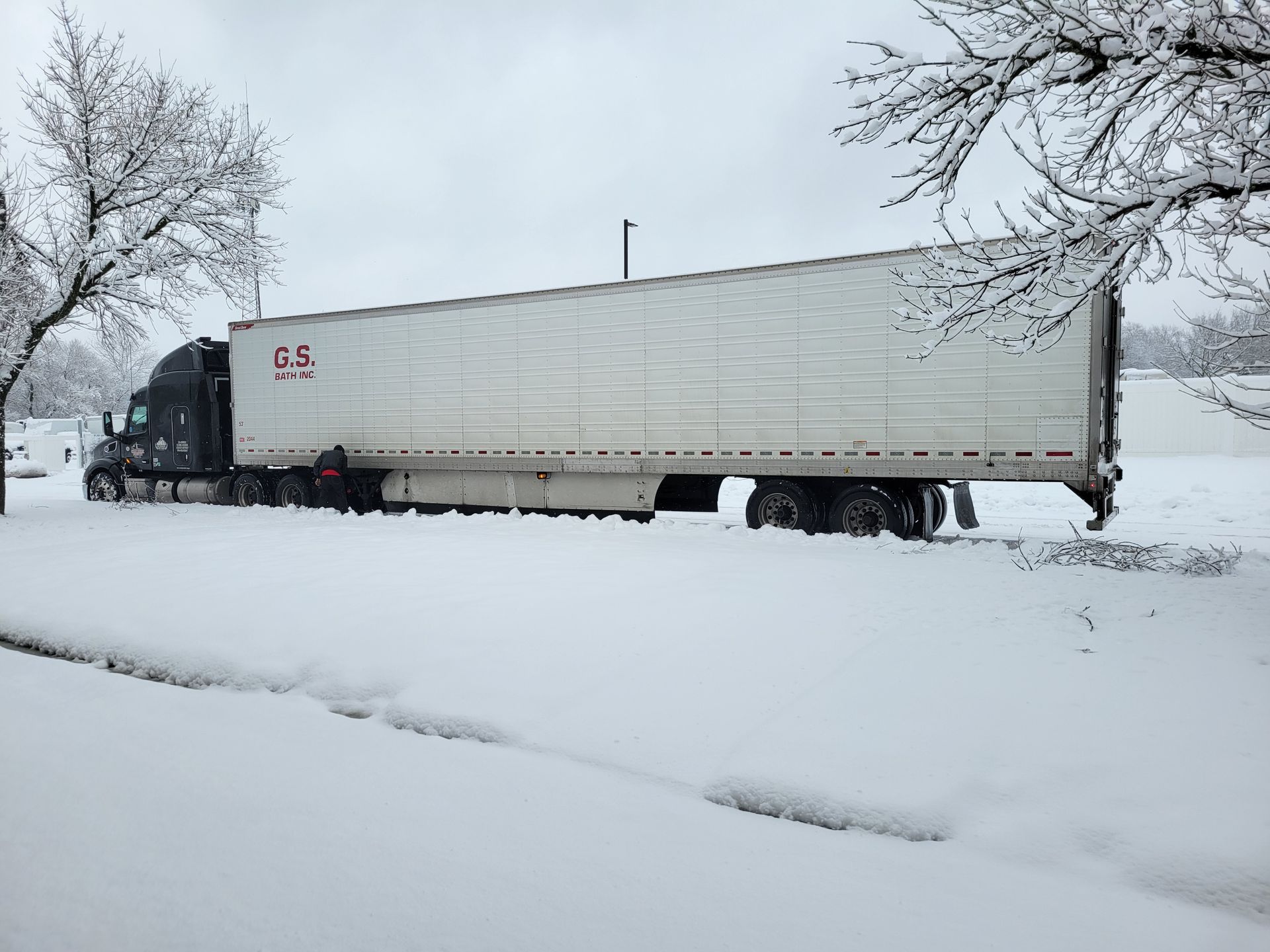 A semi truck is parked in the snow on a snowy day.
