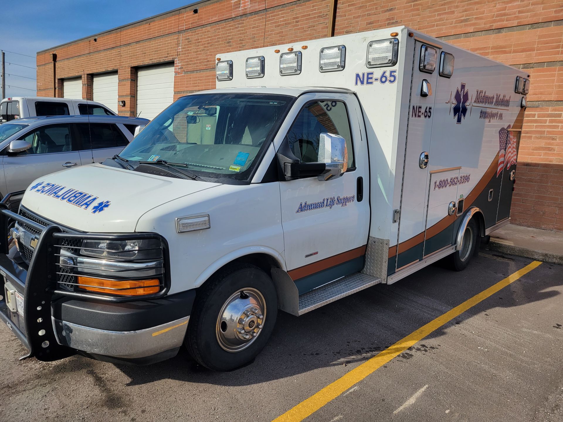 A white ambulance is parked in a parking lot in front of a brick building.