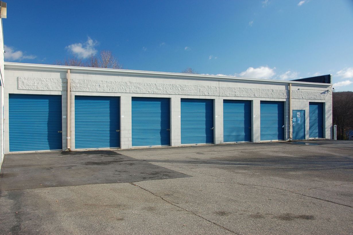 Row of white storage units with blue garage doors painted with wavy patterns, under a blue sky.