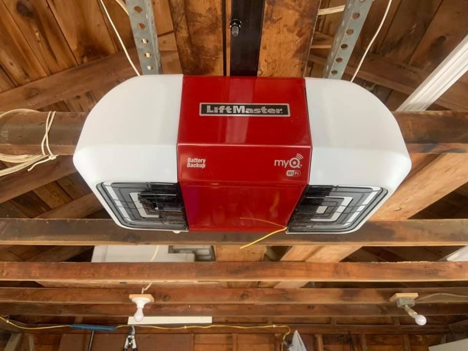 A LiftMaster garage door opener, red and white, mounted on wooden rafters in a garage.