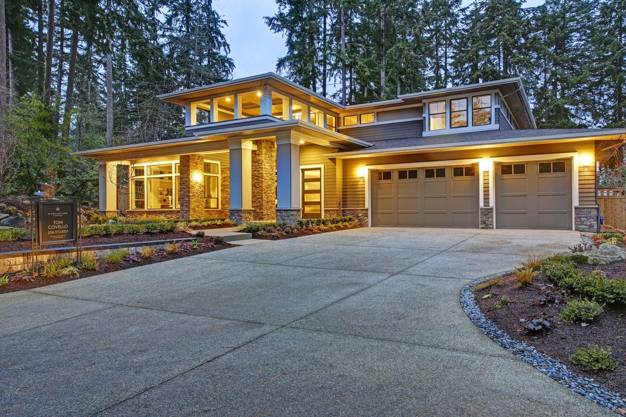Modern home with a stone and wood exterior, two-car garage, and long concrete driveway. Surrounded by trees.
