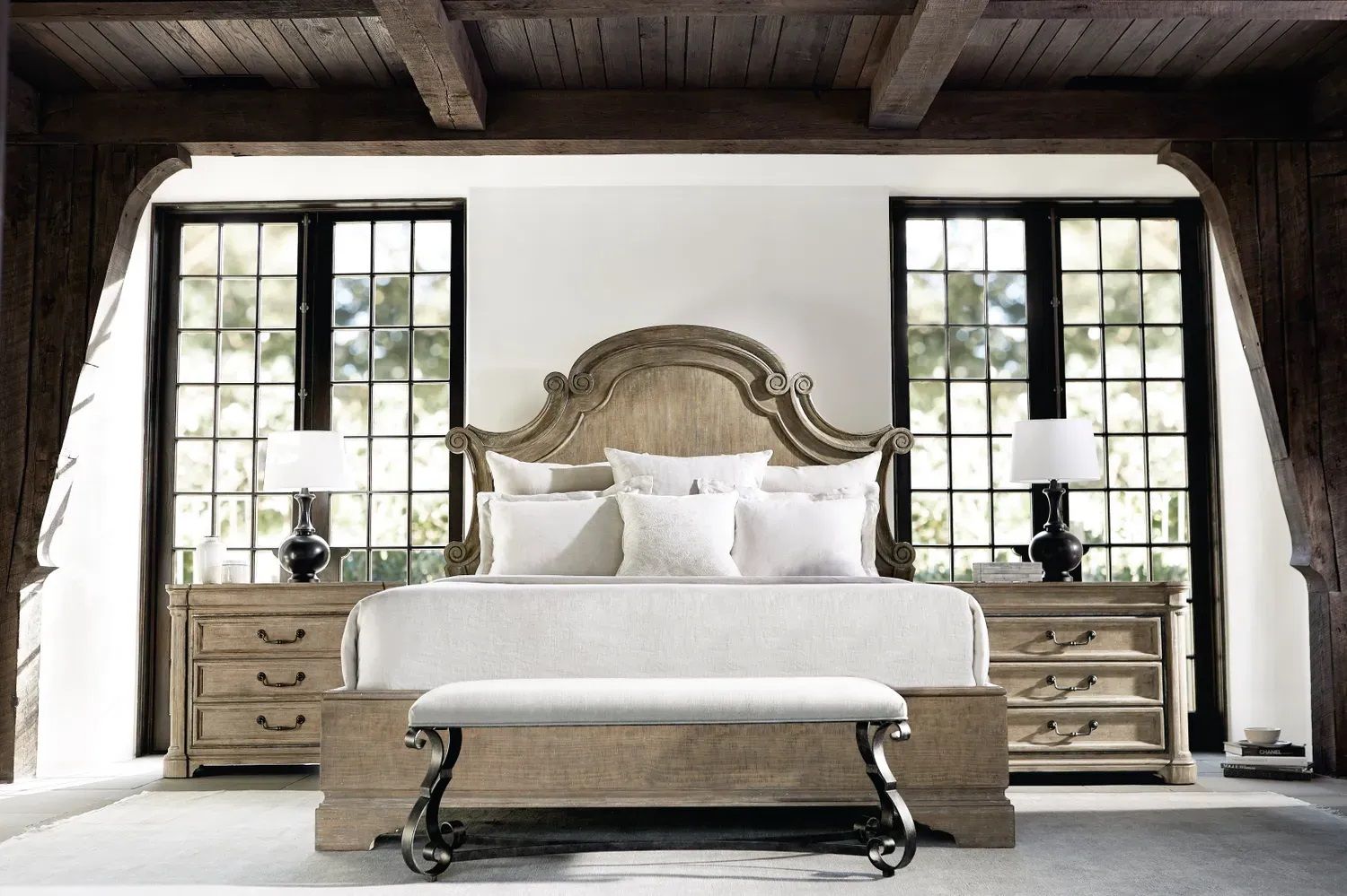 A bedroom with a bed, nightstands, lamps, and a bench.