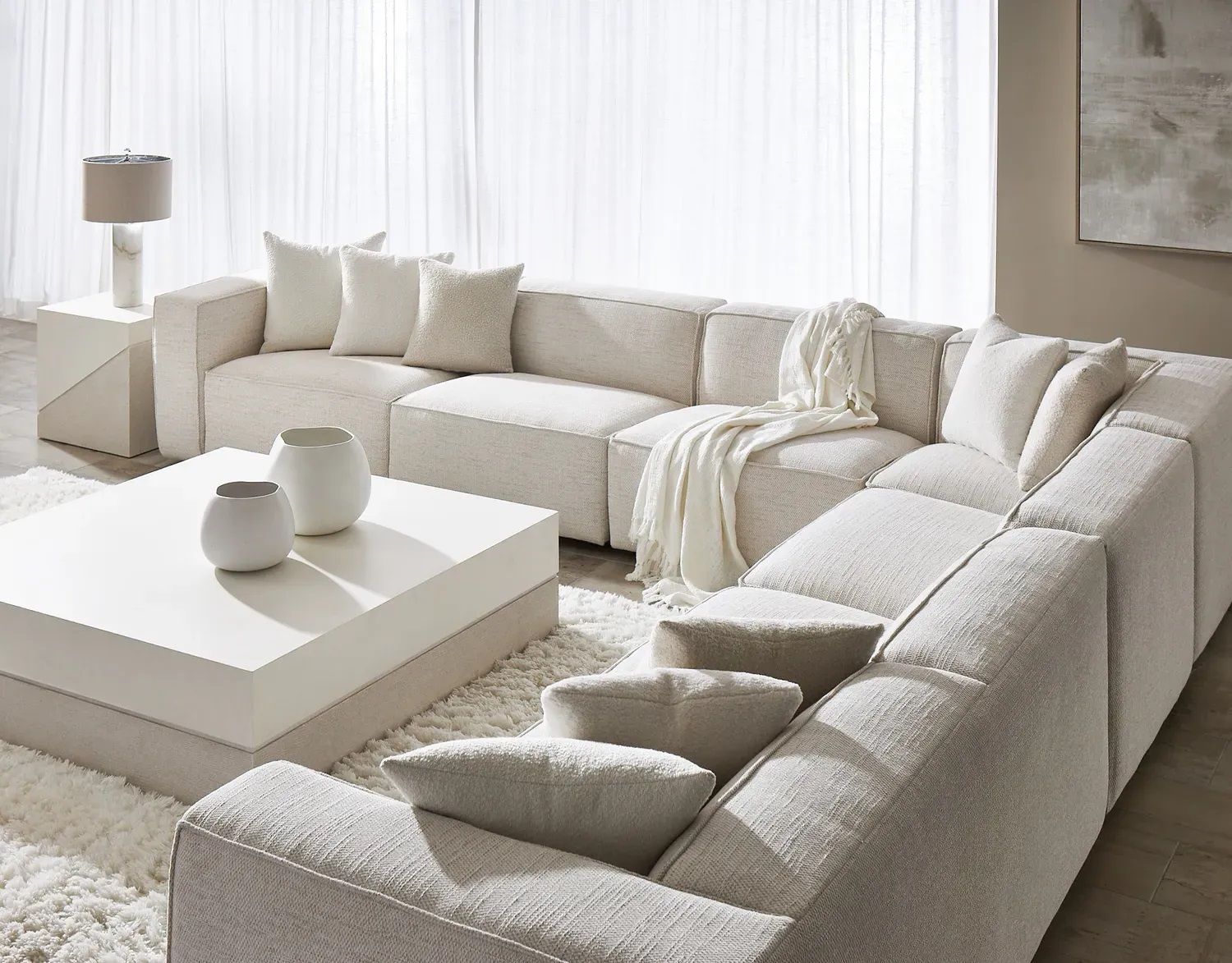 A living room with a large white sectional couch and a white coffee table.