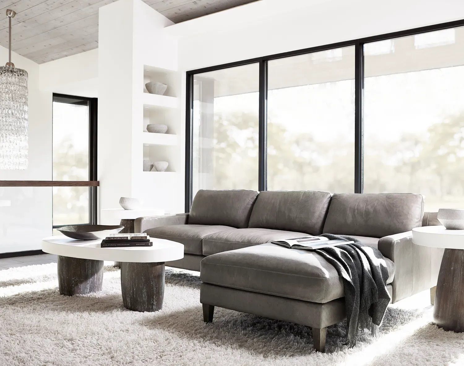 A living room with a couch, ottoman, coffee table, and large windows.