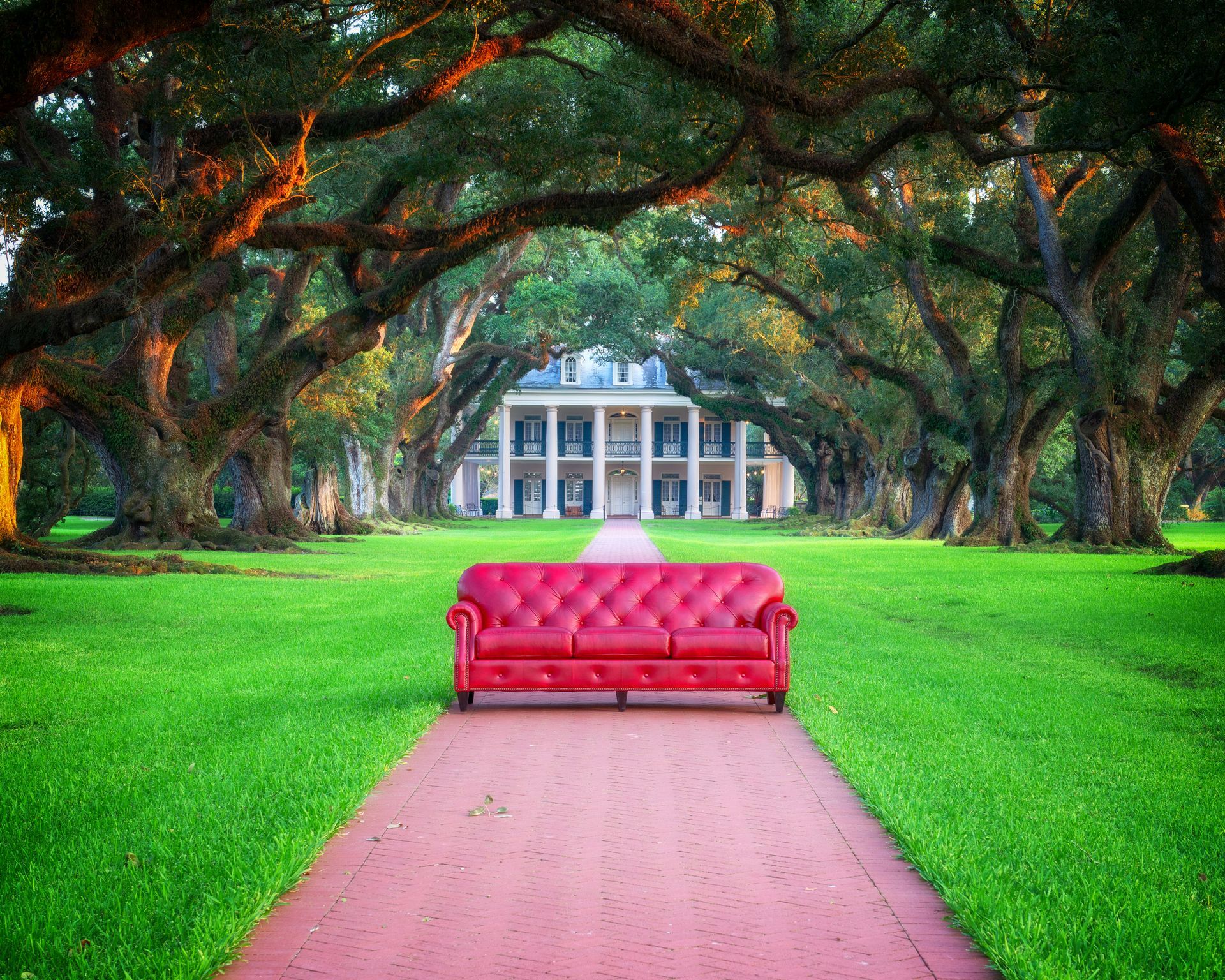 A red couch is sitting on a path in front of a large house