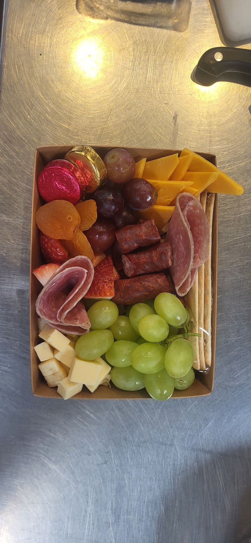 Assorted sliced fruits arranged in a clear container on a countertop, including grapes, strawberries, and melons