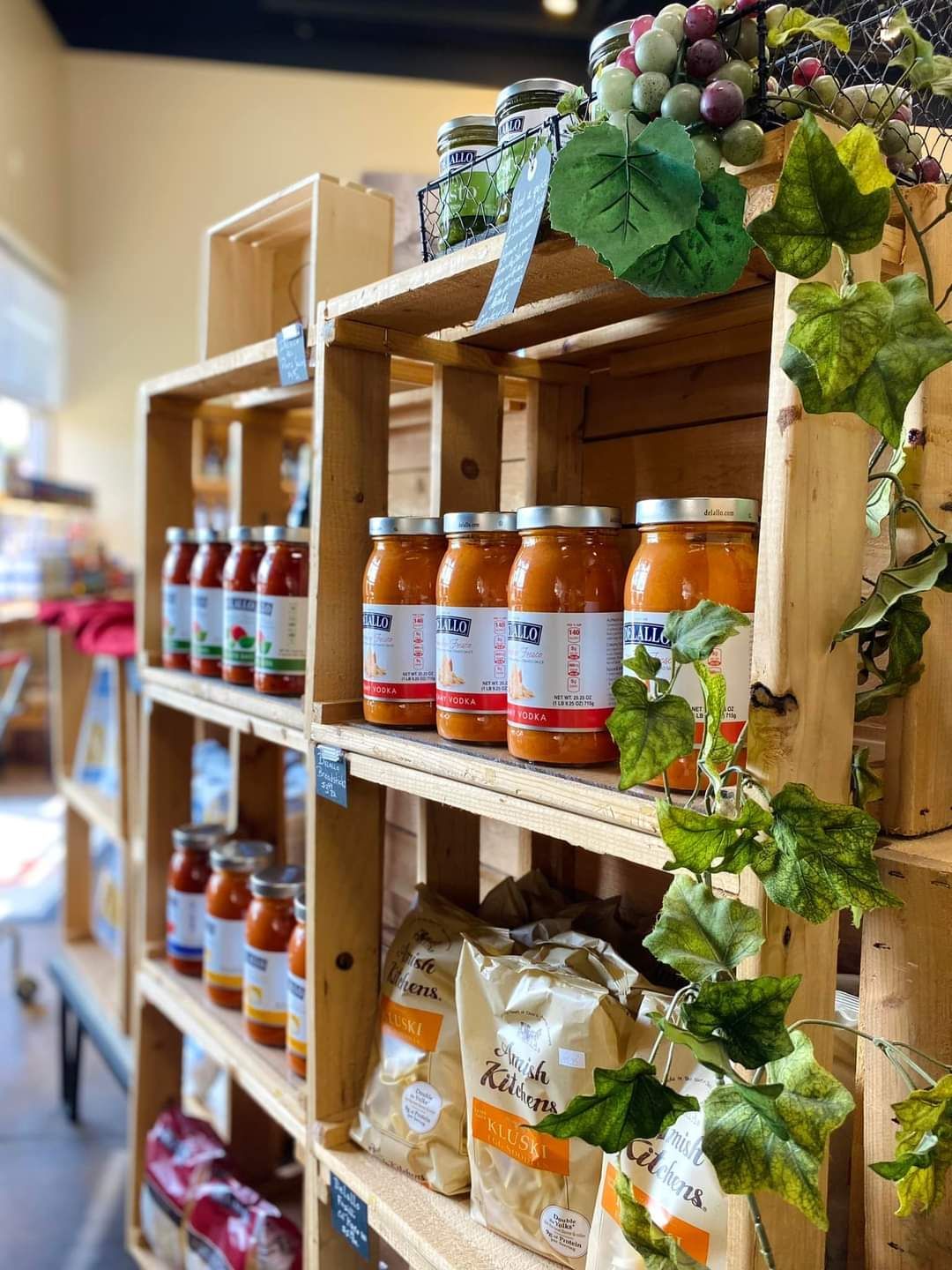 Shelves of packaged foods and jars in a warmly lit grocery store aisle, with hanging grapes on top.