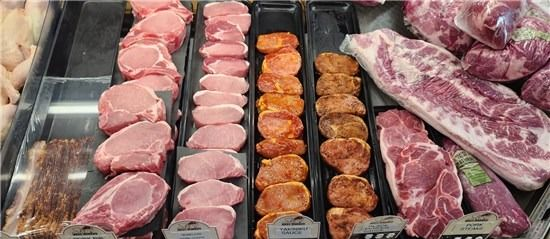 Assorted raw cuts of meat displayed in a refrigerated deli case.