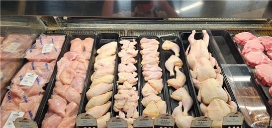 Butcher case with trays of raw chicken cuts and whole chickens arranged behind glass.