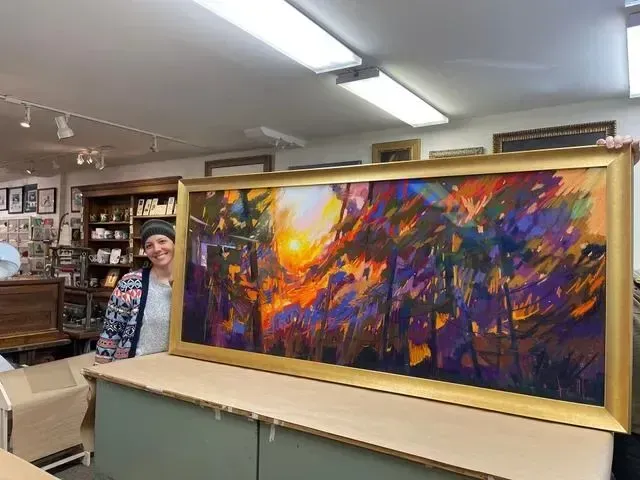 Framed abstract painting with orange, purple, and blue colors displayed in a gallery or shop.