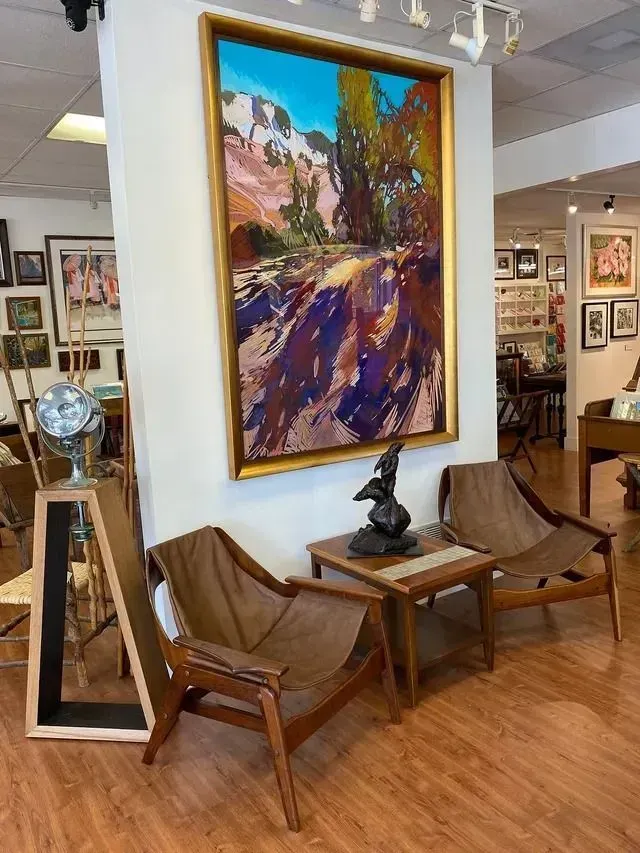 Art gallery seating area with abstract painting, wooden chairs, small tables, and framed artworks on the walls.