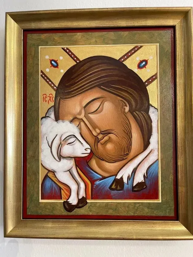 Framed icon of Jesus embracing a white lamb, with cross halo and gold background.