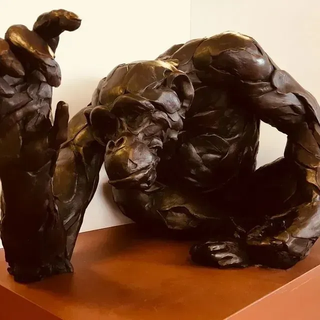 Dark bronze abstract sculpture on a wooden base, with two intertwined human-like forms.