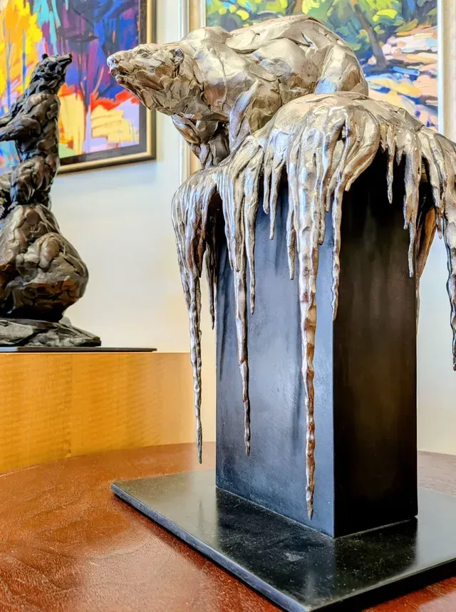 Abstract sculpture in gallery, with a dark pedestal and draped metallic forms hanging over the sides.