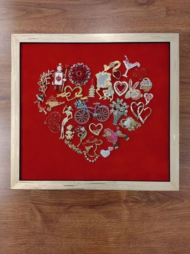 Red heart-shaped collage of jeweled flowers and hearts in a silver frame on a wooden surface.