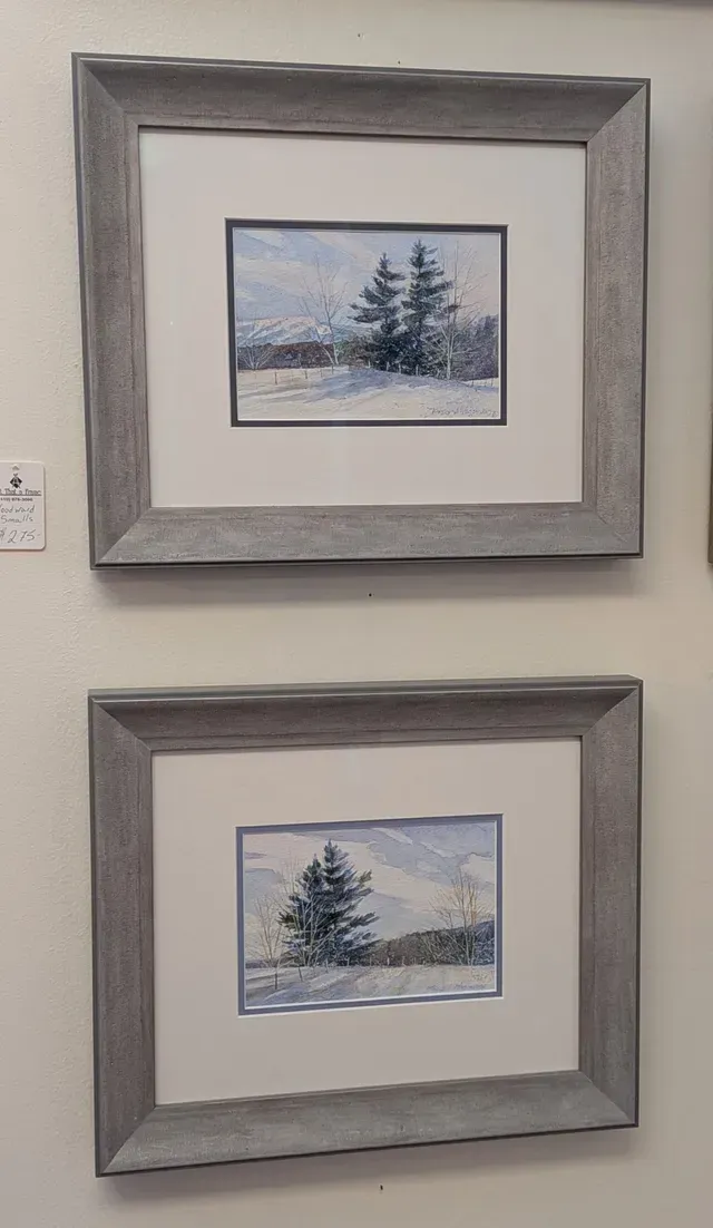 Two framed winter landscape prints with gray mats hanging on a wall.