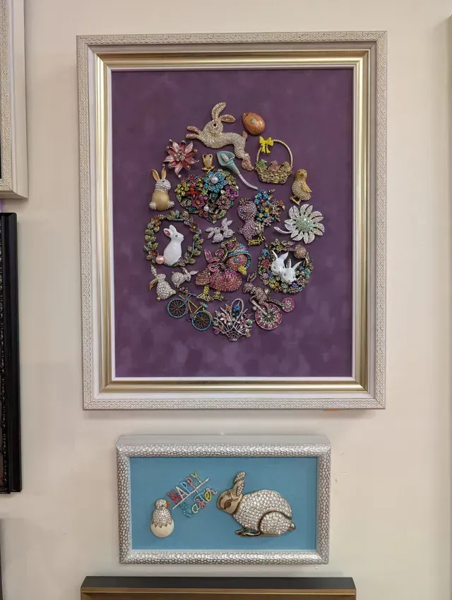 Two framed jeweled artworks on a wall, one purple and one blue with a silver rabbit.