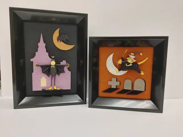 Two framed Halloween shadow boxes with witches, a moon, and orange pumpkin scenes.