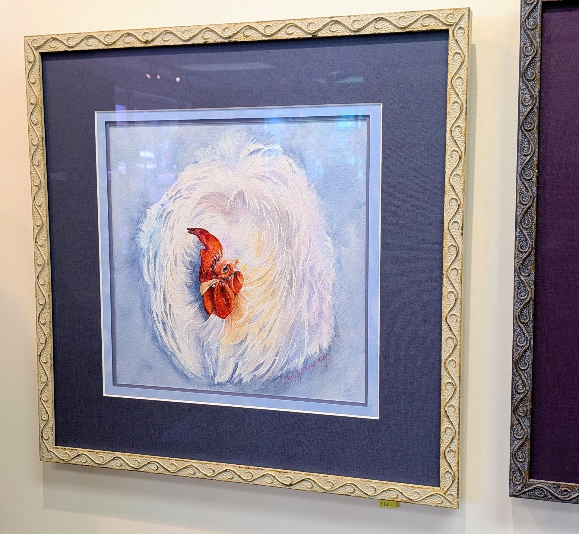 Framed abstract painting with white and blue brushstrokes and a red-orange center on a wall.