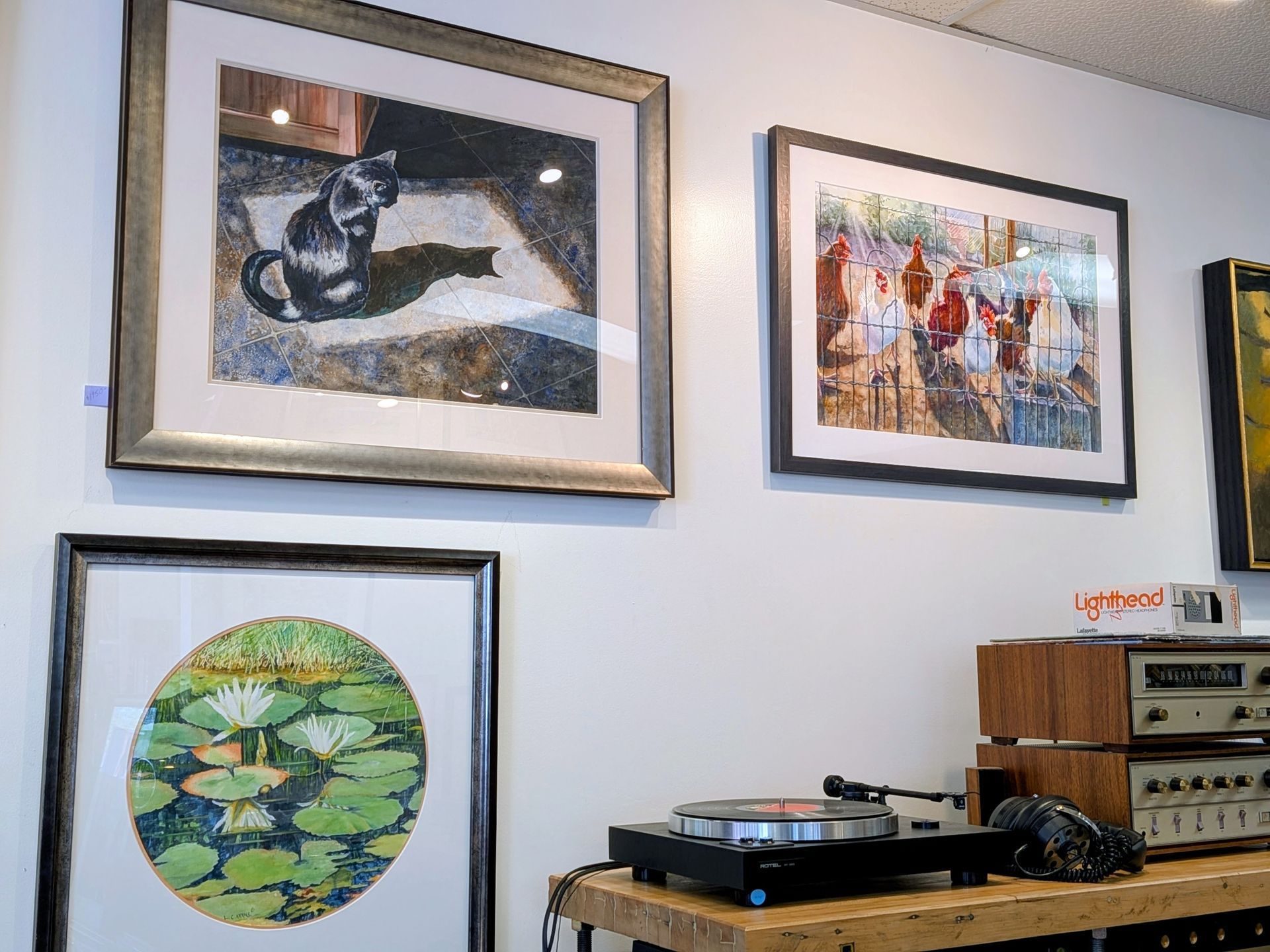 Framed artwork on a wall above a turntable and stereo equipment, with a circular green print below.