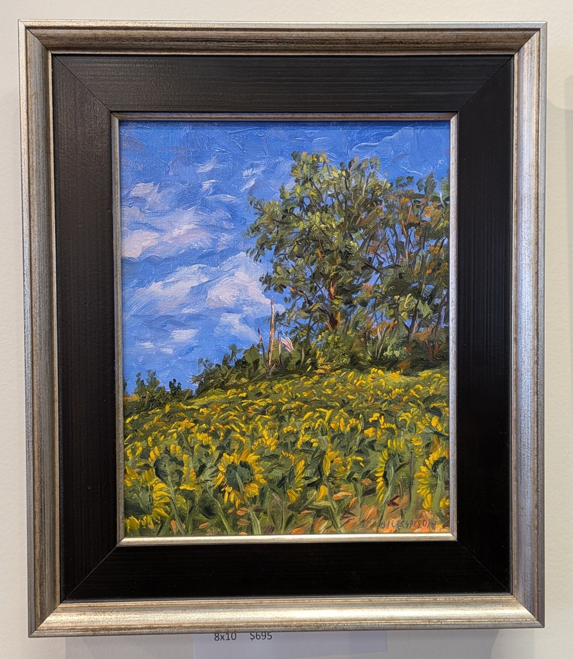 Framed painting of a sunny hillside with yellow wildflowers, a tree, and a blue sky with clouds.