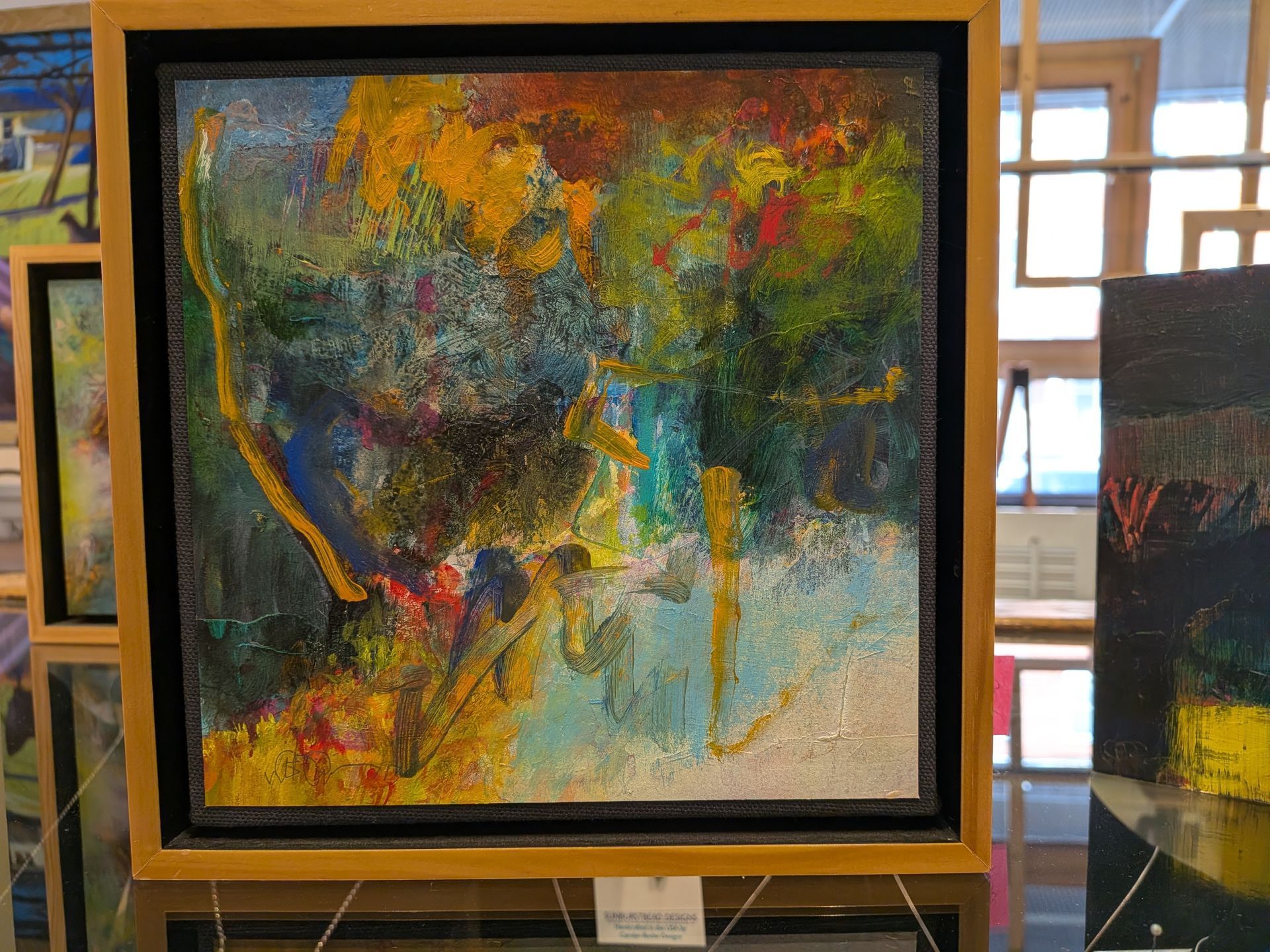 Abstract colorful painting in a gold frame with dark green, yellow, orange, and teal tones.