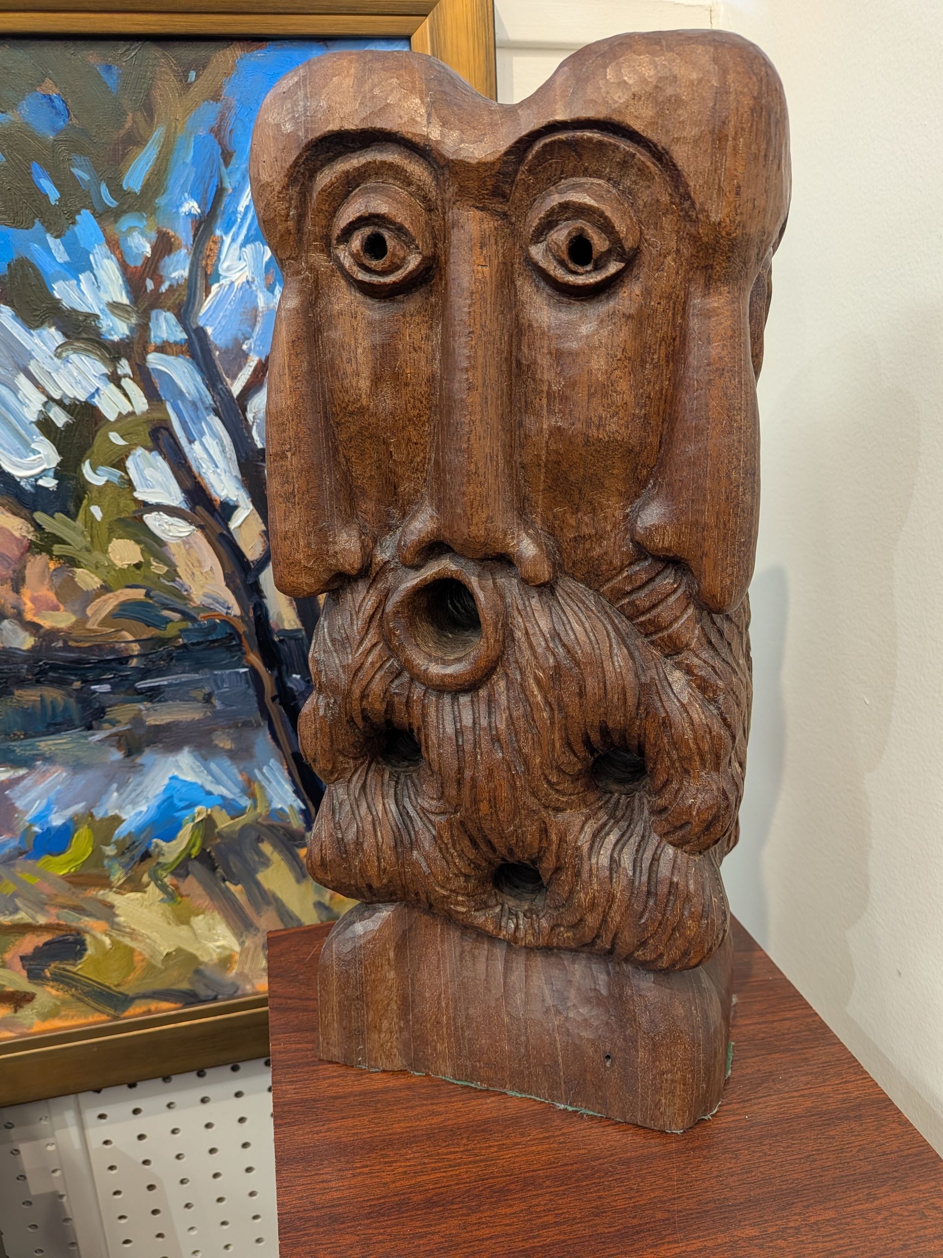 Rustic wooden owl sculpture with large eyes on a shelf beside a colorful painting.