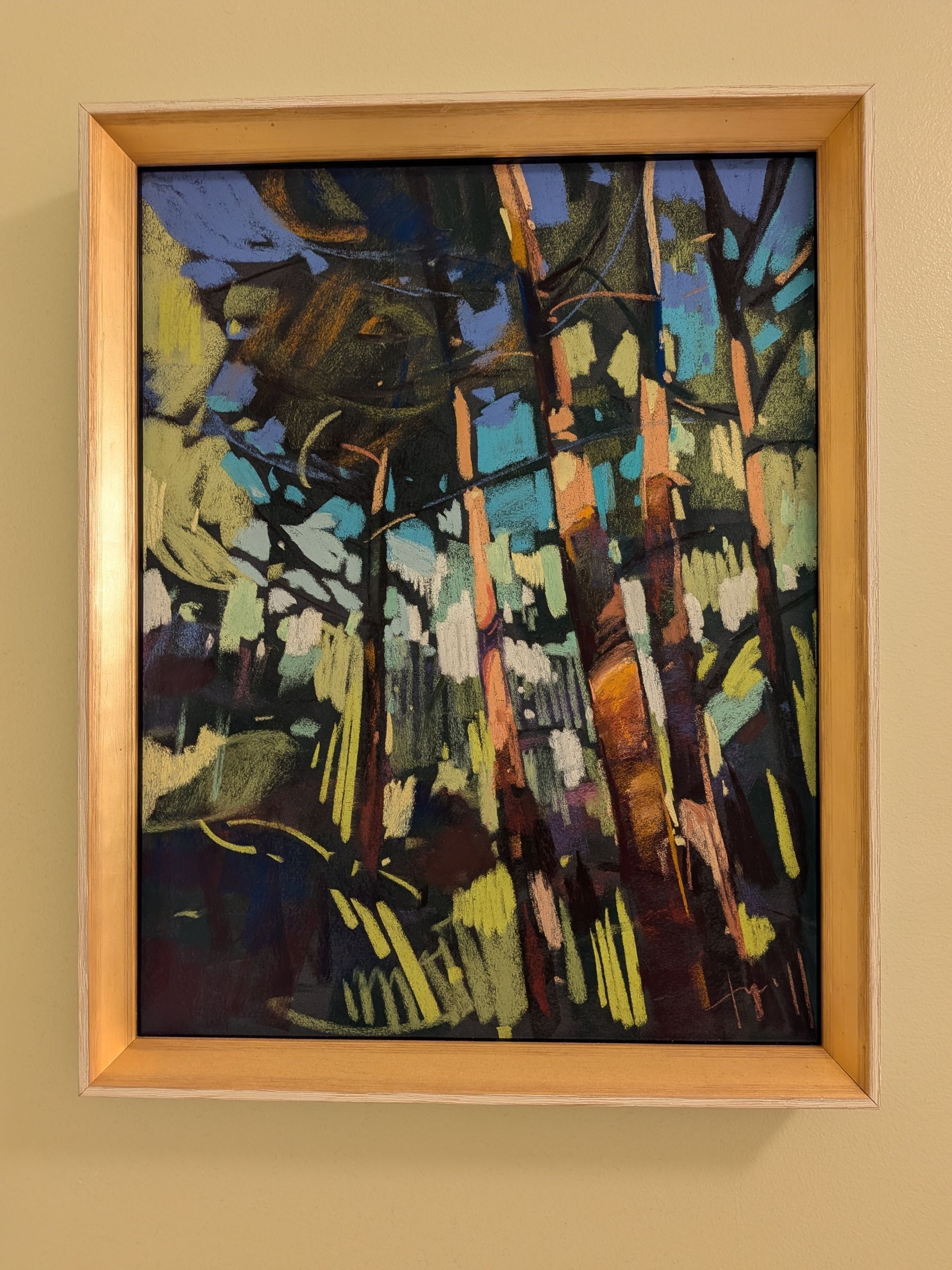 Framed abstract painting of colorful trees and sunlight in a forest scene.