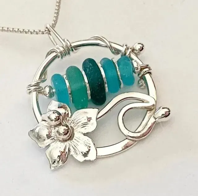 Silver flower pendant necklace with turquoise beads on a chain.
