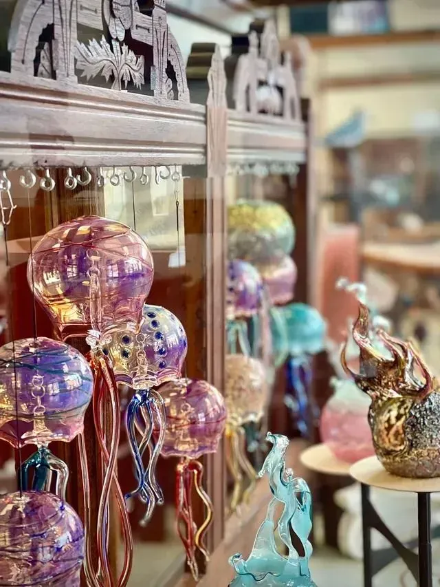 Colorful glass animal figurines and ornaments displayed on shelves in a shop window.