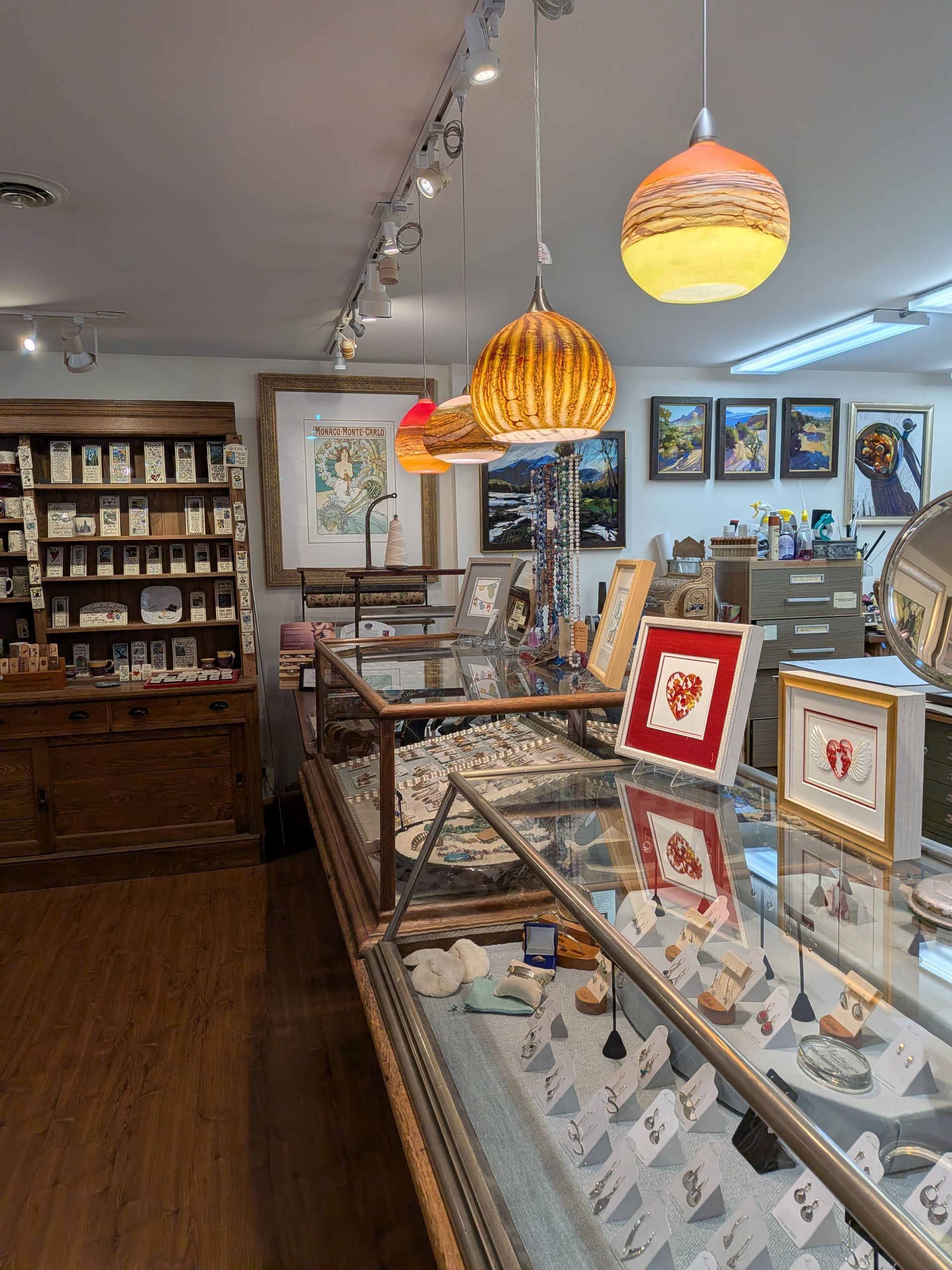 Art gallery with glass display cases, framed artworks, and hanging pendant lights in a cozy interior.