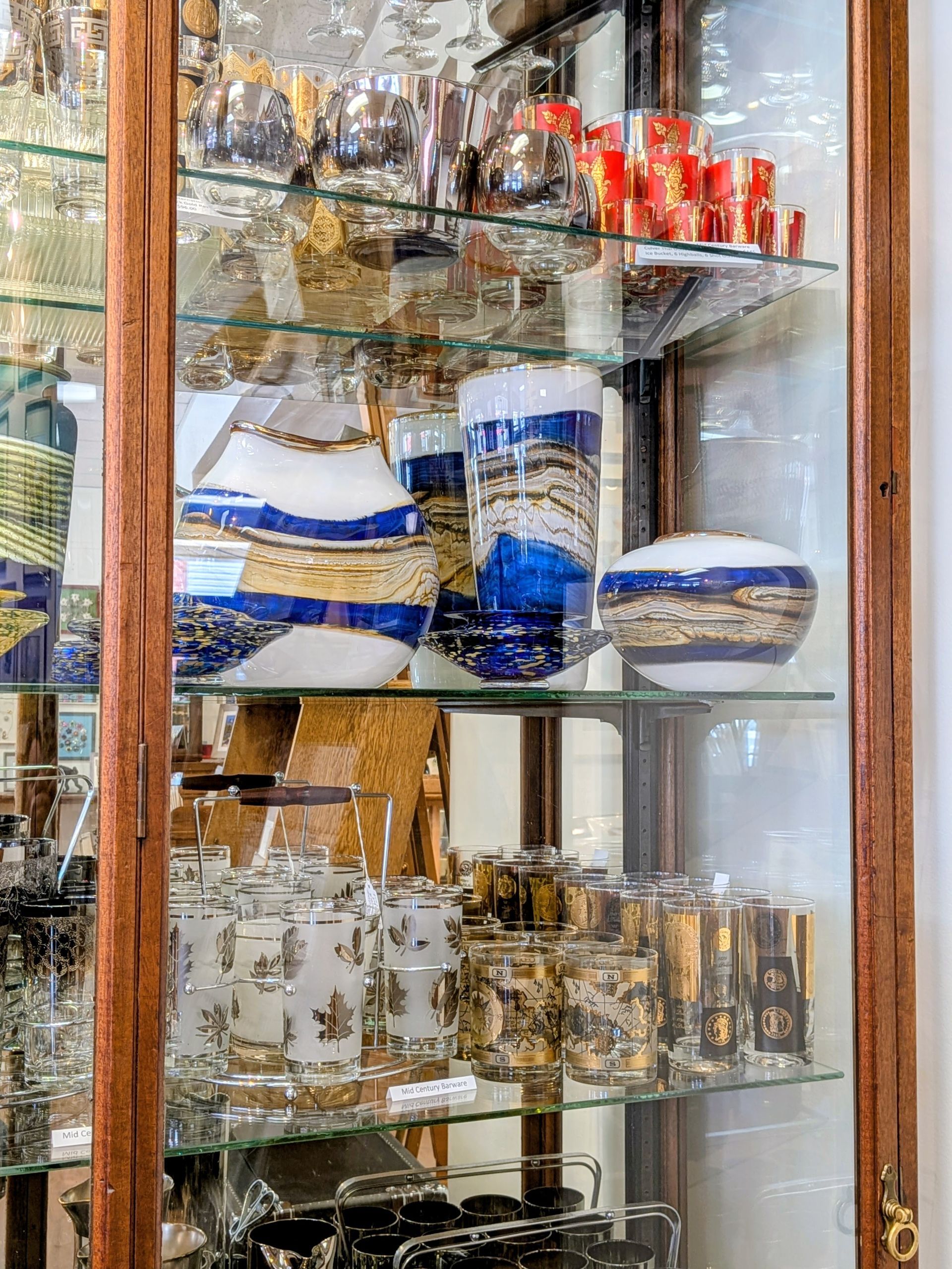 Glass display cabinet with shelves of blue-and-white cups, mugs, and decorative glassware.