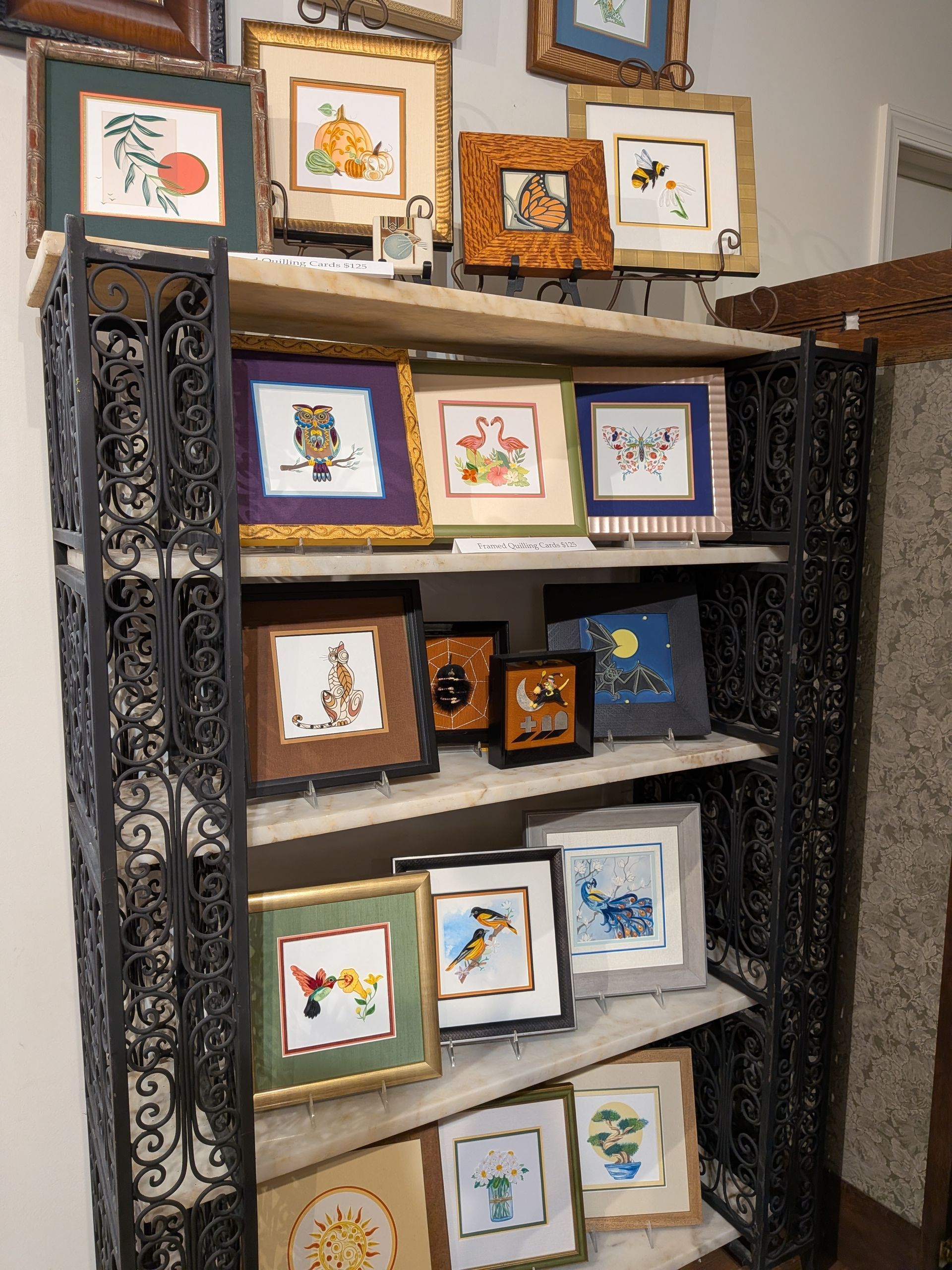 Decorative framed art prints displayed on a black metal shelf in a home interior.