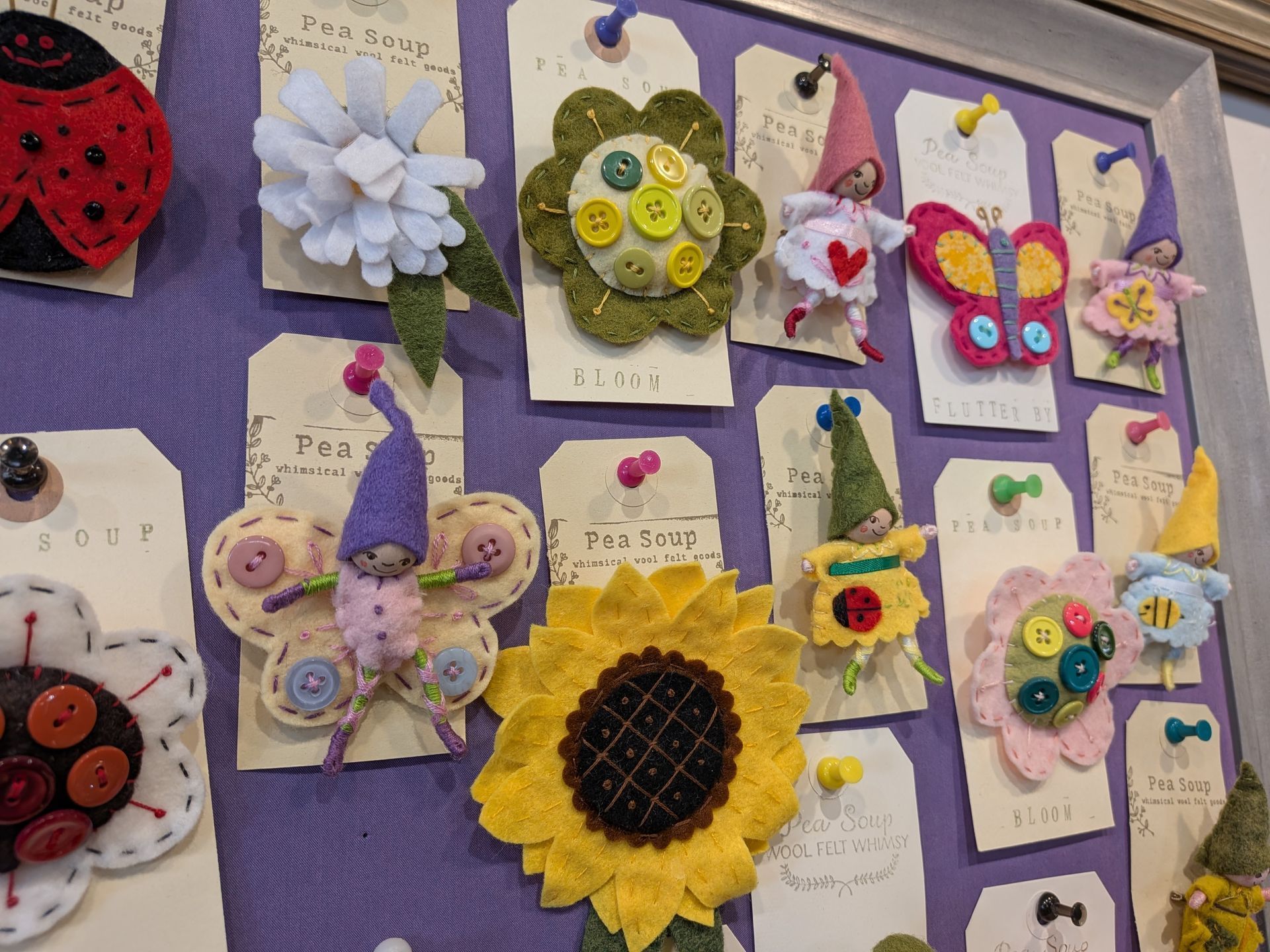 Colorful butterfly and flower crafts pinned on a purple bulletin board, including a sunflower and ladybug art.