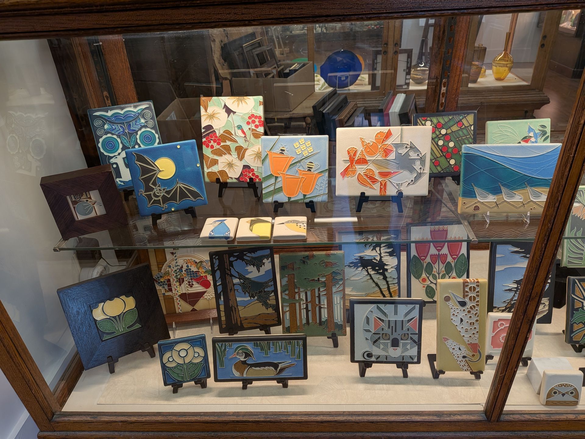 Colorful small paintings displayed in a shop window on easels and shelves.